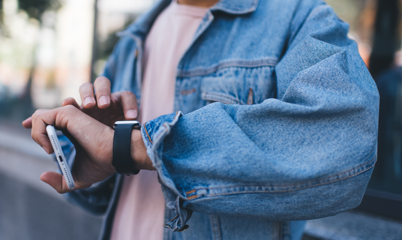 Mann schaut auf seine Smartwatch und scrollt, während er in der anderen Hand sein Handy hält