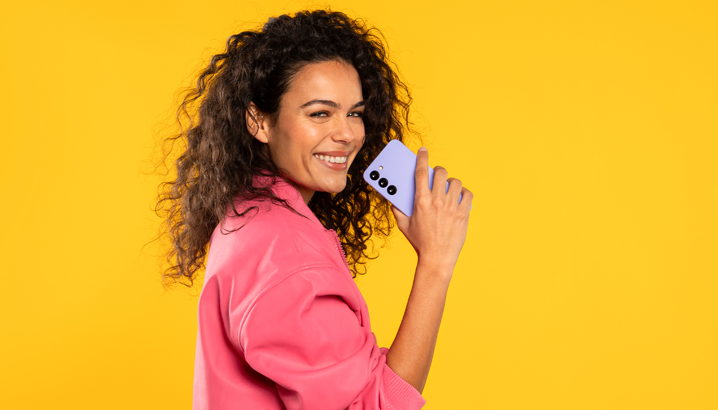 Eine Frau hält lachend eine lila Handyhülle, der Hintergrund ist gelb.