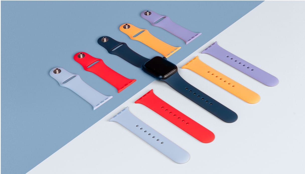 Du siehst eine Apple Watch in Midnight mit einem dunkelblauem Armband. Daneben liegen weitere Armbänder in verschiedenen Farben stilisiert ausgerichtet. Der Untergrund ist zur Hälfte blau, zur Hälfte weiß.