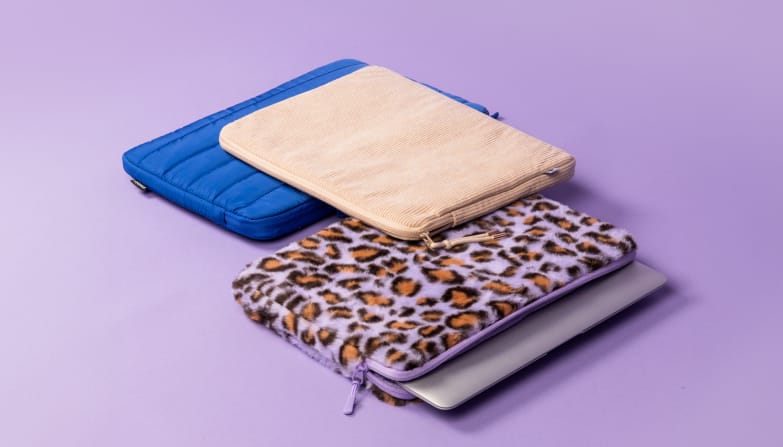 Eine kobaltblaue Laptop-Hülle, eine beige Cord-Hülle und eine Laptop-Hülle mit violettem Leopardenmuster liegen nebeneinander.