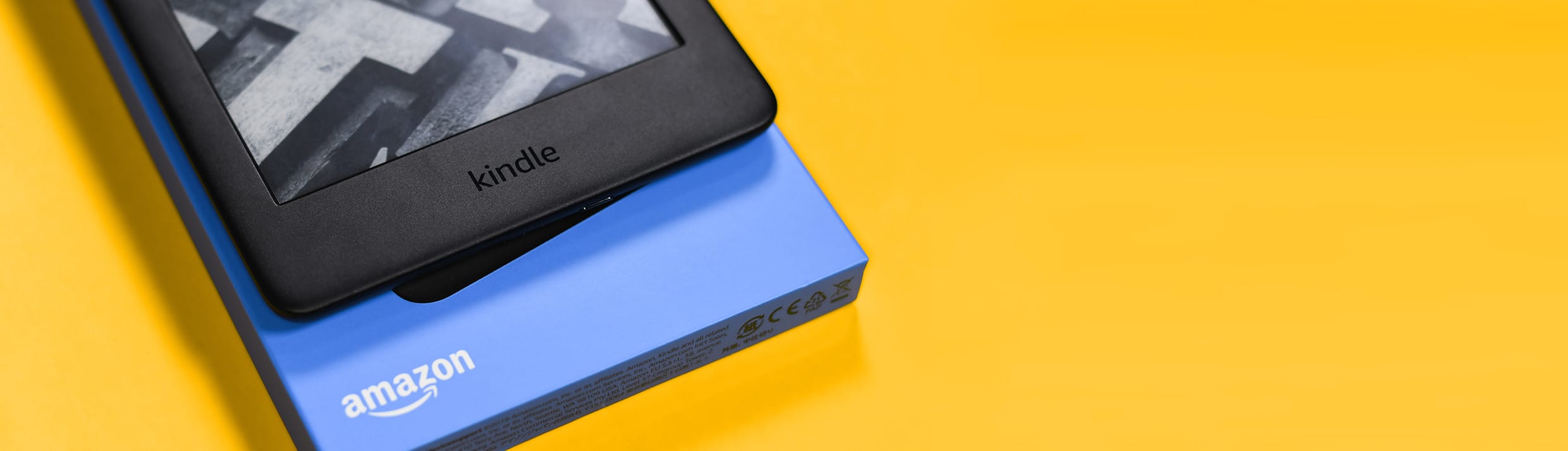 Ein Amazon Kindle und die Verpackung auf einem gelben Hintergrund