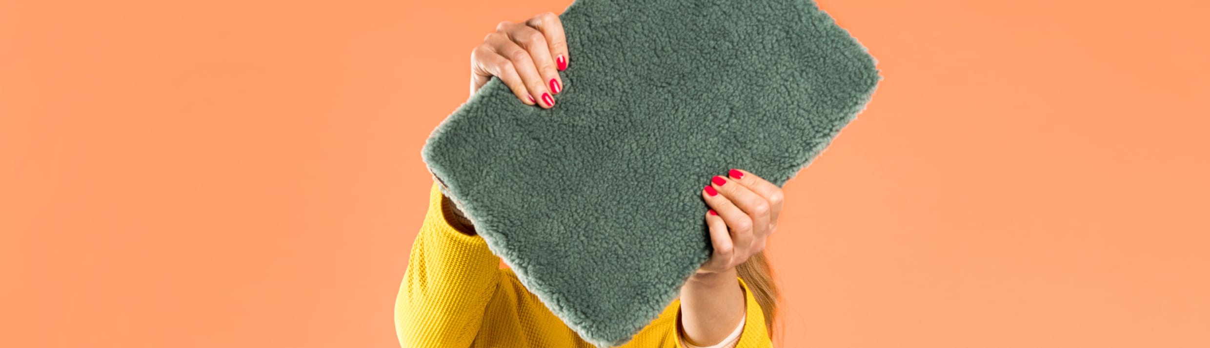 Eine Frau hält eine dunkelgrüne Laptop-Hülle aus Teddy-Stoff vor ihr Gesicht.