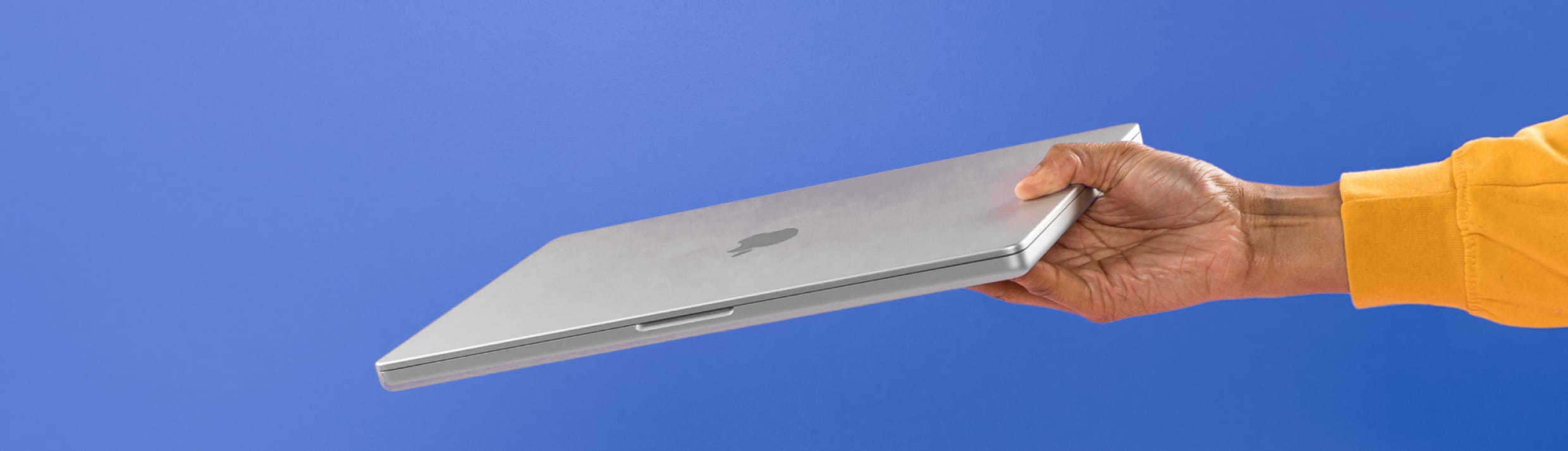 Een Hand, die ein silbernes Apple MacBook hochhält, vor einem blauen Hintergrund.