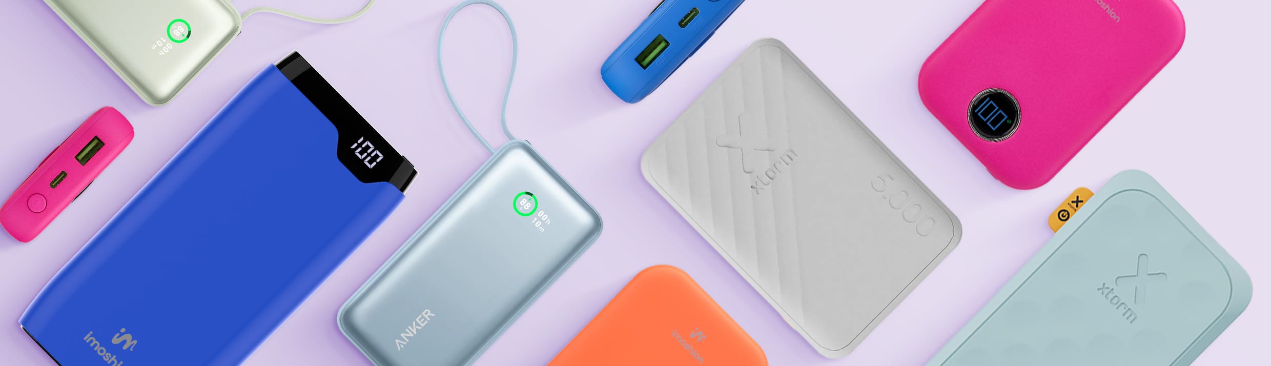 Eine Übersicht über verschiedene Marken, Größen, Farben und Arten von Powerbanks, einige liegen, andere stehen auf der Seite. Unter anderem Powerbanks von Anker, Xtorm und imoshion, auf einem hellvioletten Hintergrund.