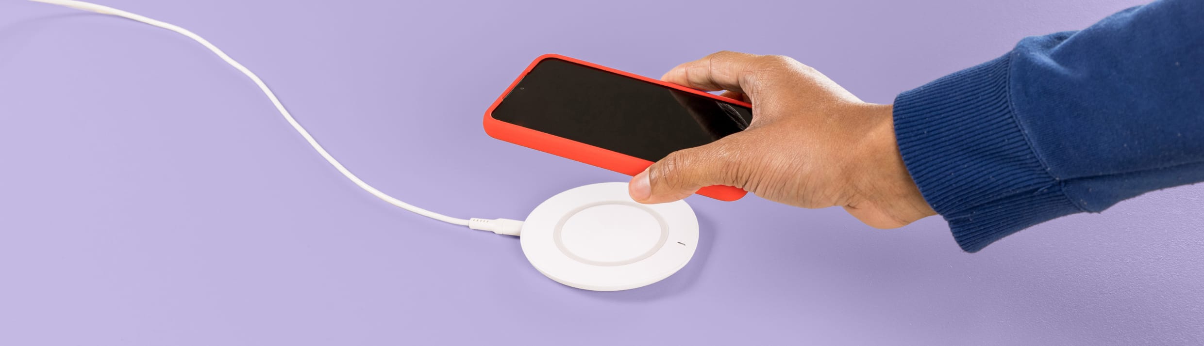 Een hand komt van rechts en legt een telefoon op een draadloze oplader.