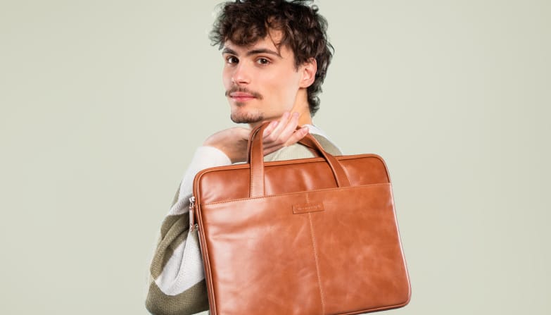 Ein Mann hält eine Laptoptasche aus cognacfarbenem Leder in seinen Händen.