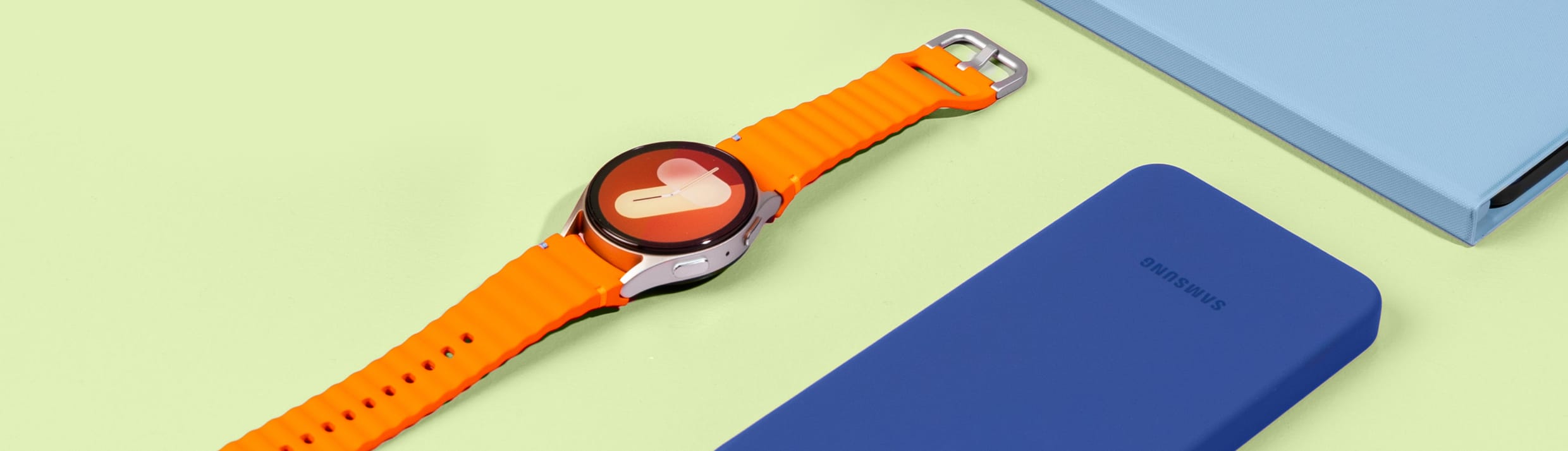 Foto van een Samsung Galaxy Watch met oranje bandje op een gele achtergrond. 