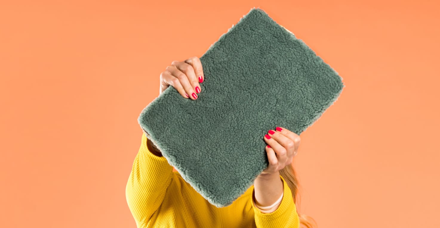 Eine Frau hält eine dunkelgrüne Laptop-Hülle aus Teddy-Stoff vor ihr Gesicht.