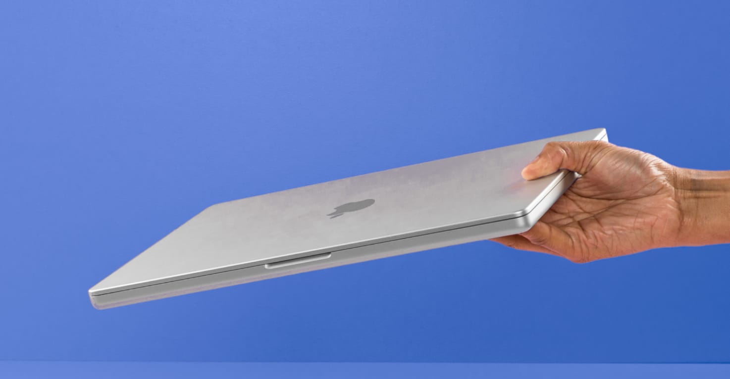 Een Hand, die ein silbernes Apple MacBook hochhält, vor einem blauen Hintergrund.