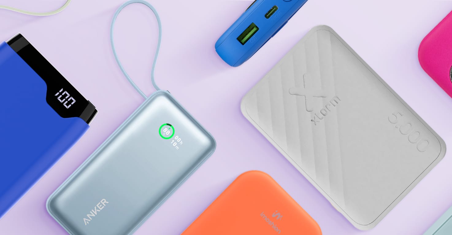 Eine Übersicht über verschiedene Marken, Größen, Farben und Arten von Powerbanks, einige liegen, andere stehen auf der Seite. Unter anderem Powerbanks von Anker, Xtorm und imoshion, auf einem hellvioletten Hintergrund.