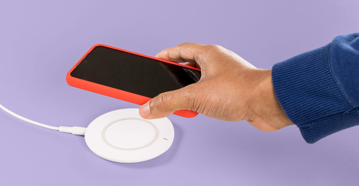 Een hand komt van rechts en legt een telefoon op een draadloze oplader.