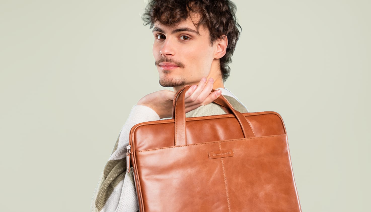 Ein Mann hält eine Laptoptasche aus cognacfarbenem Leder in seinen Händen.