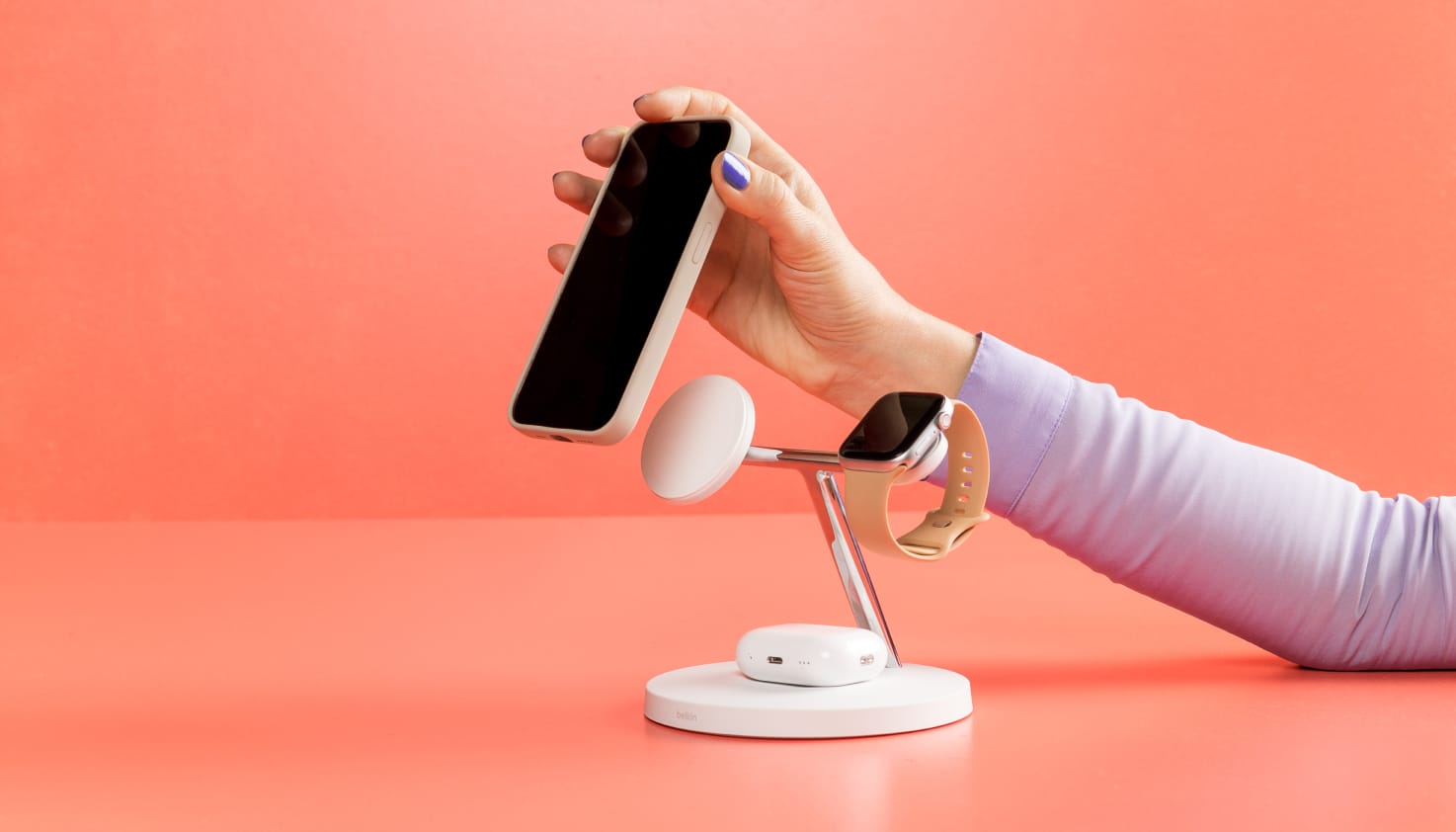 Een hand komt van rechts en klikt een telefoon magnetisch op een oplaadstation.